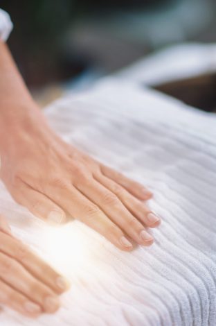 Female therapist performing Reiki therapy treatment holding hands over woman's stomach. Alternative therapy concept of stress reduction and relaxation.